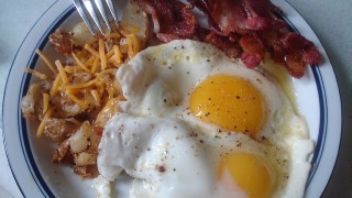 Bacon and eggs plus home fries with cheese on a plate